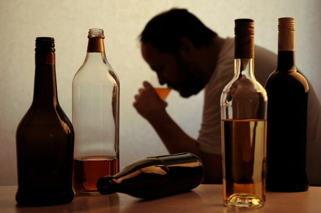 alcohol addiction concept: silhouette of drunk man drinking behind bottles