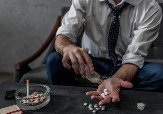 businessman with drug addiction pouring pills on hand from bottle